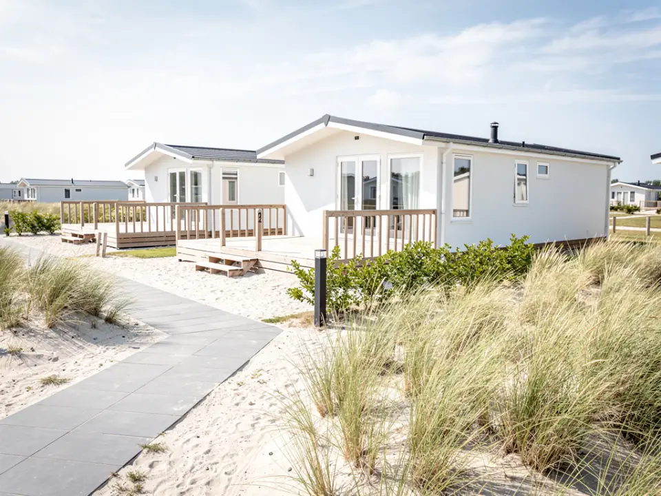 Rij schone witte chalets met houten vlonders op een duinpark