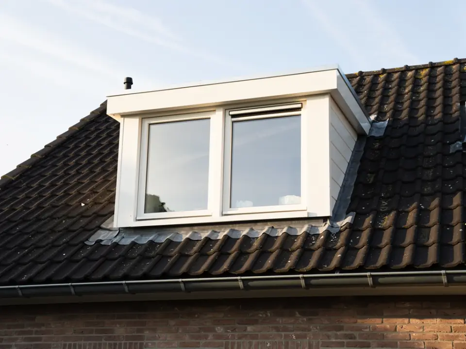 Schone dakkapel met helderwitte panelen, schone ramen en een lege goot